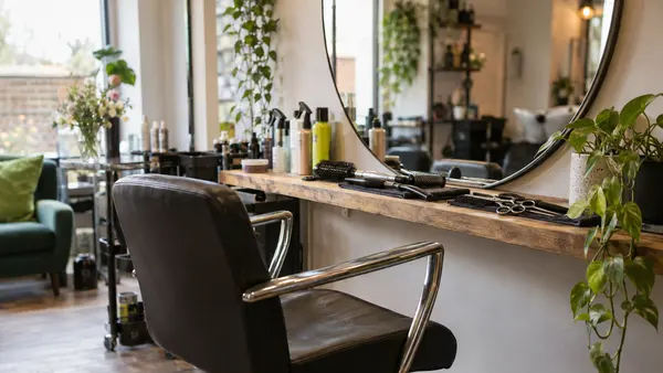 An empty salon chair and mirror with scissors and combs on the counter.
